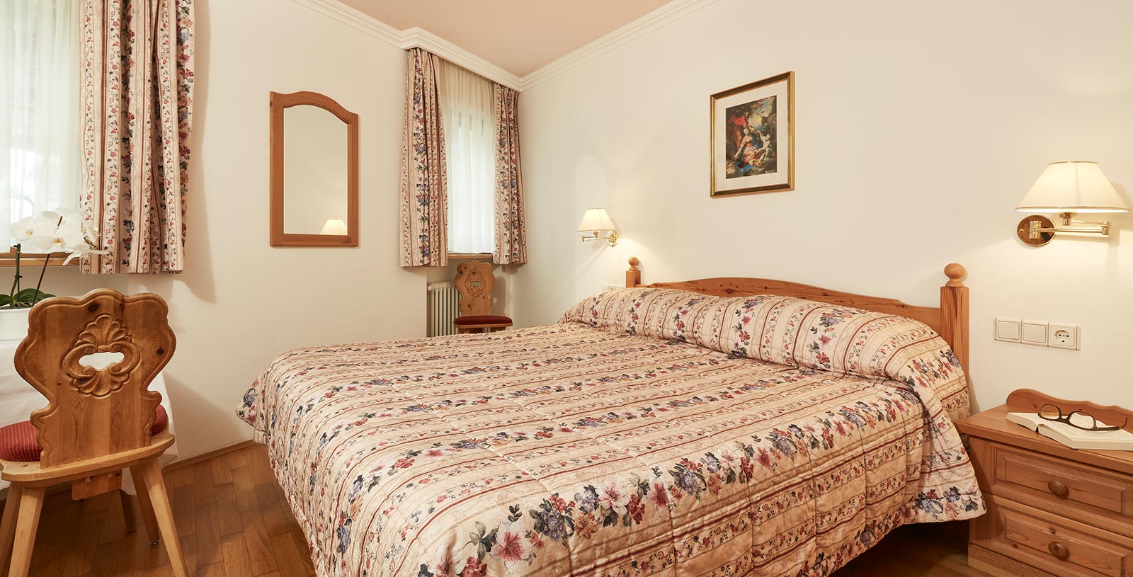 the kingsize bed of a vacation home in Corvara, curtains and bed linen wear the same flower motif